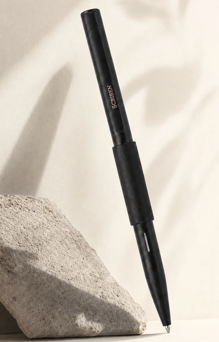 The Scriben pen in matte black, resting against a stone